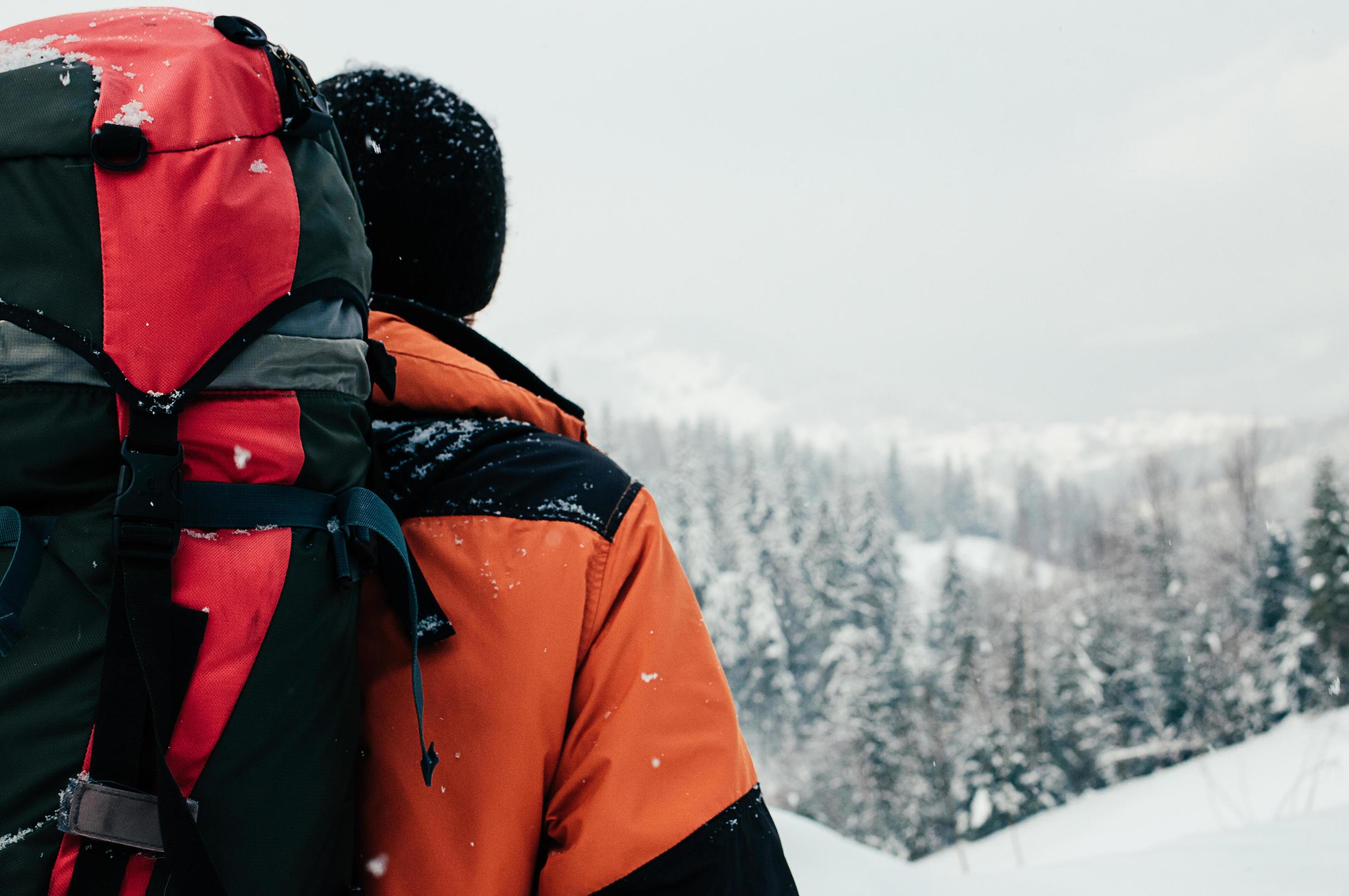 achteraanzicht van toeristische man genieten van berg boslandschap op besneeuwde winterdag. oranje kledingstuk, rode rugzak. wandelen reizen extreme levensstijl concept foto