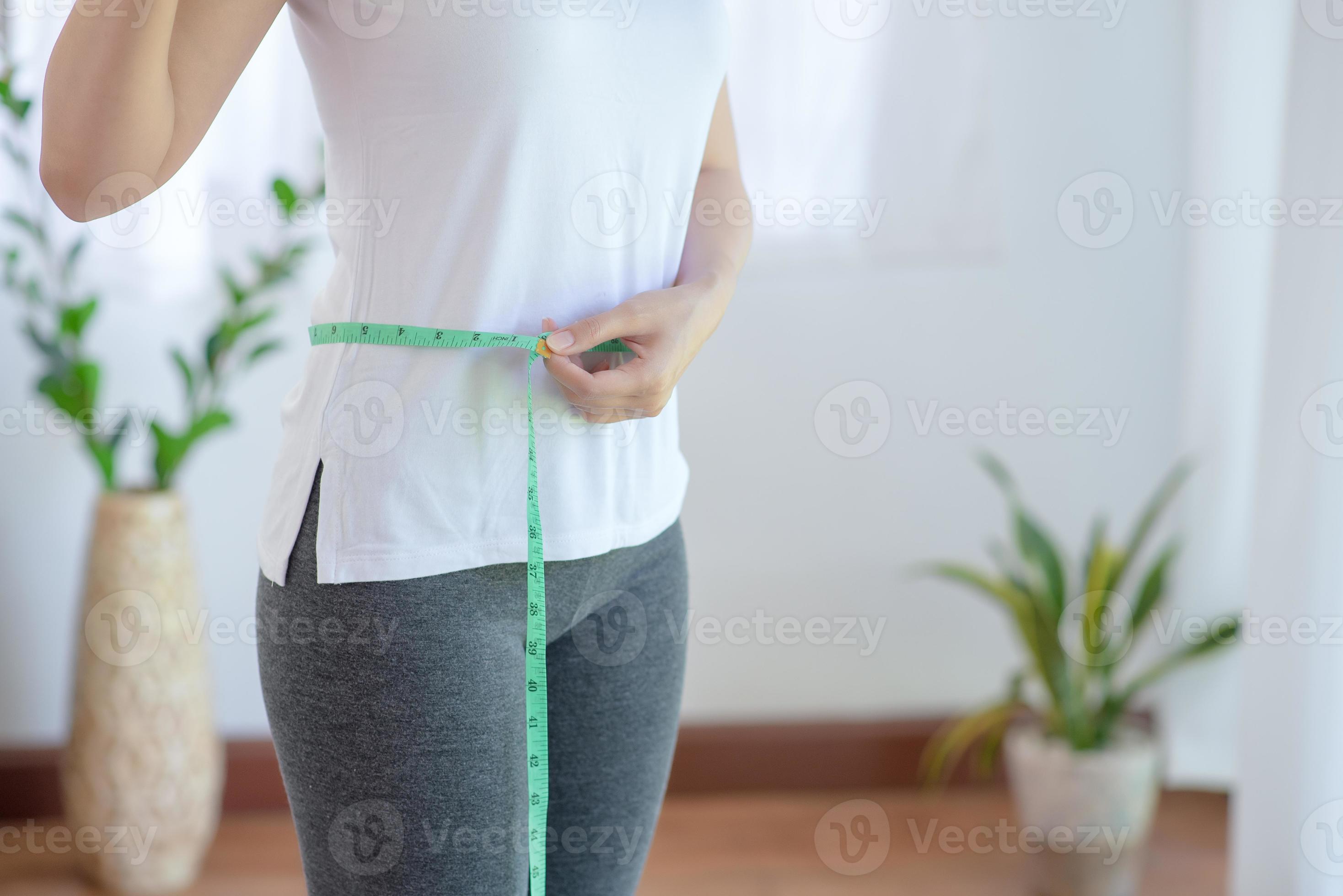 elke keer aan de andere kant, houten sportieve vrouw blijft sporten met gezonde voeding haar slanke lichaam en  dunne taille meten met een meetlint. 4849999 Stockfoto