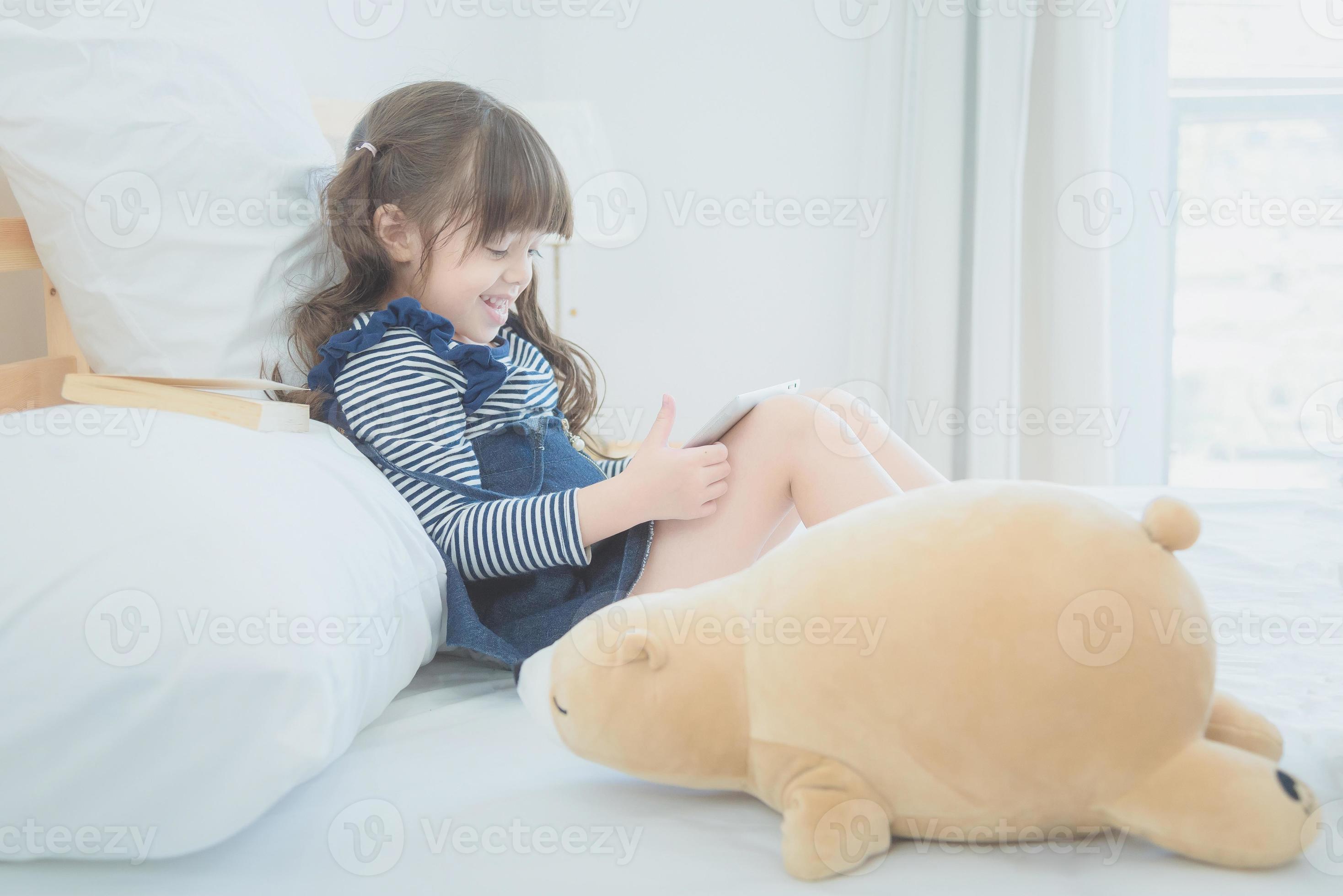 Daarom Alsjeblieft kijk Metropolitan schattig klein meisje geniet van het kijken naar tekenfilms op slimme tablet  met schattige pop terwijl ze thuis op bed in de kinderkamer zit 4886452  stockfoto bij Vecteezy