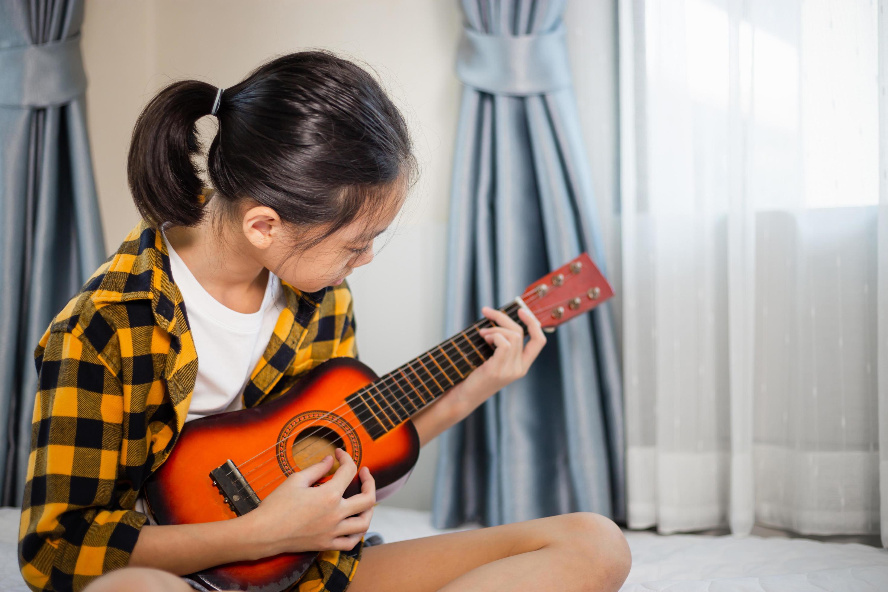 venster rijkdom jogger klein meisje speelt gitaar, kindmeisje leert gitaar spelen in de  slaapkamer, hobby voor kinderen 6637339 Stockfoto