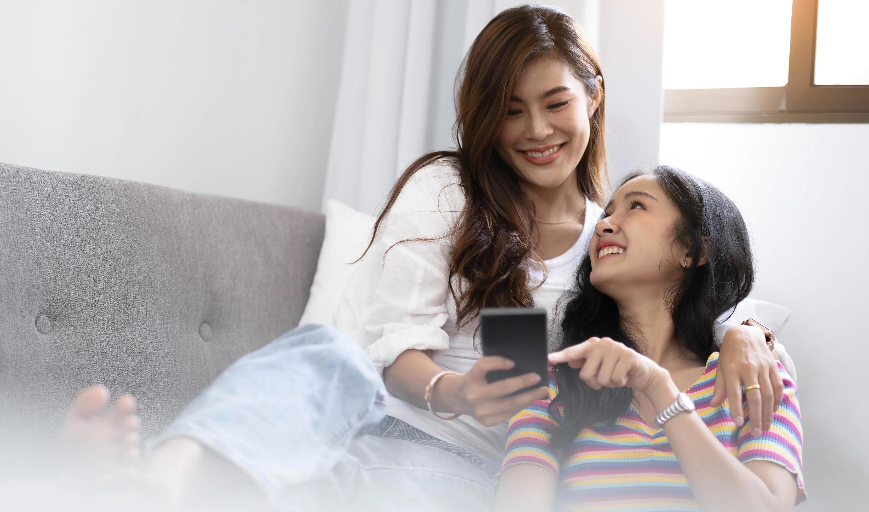 jonge mooie Aziatische vrouwen lesbisch koppel minnaar met behulp van smartphone video-oproep online in de woonkamer op de bank thuis met lachende face.concept van lgbt seksualiteit met gelukkige levensstijl samen foto afbeelding