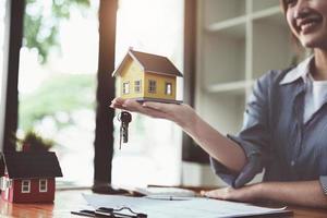 accountant, zakenvrouw, makelaar in onroerend goed, aziatische zakenvrouw die modelhuis en sleutels aan klanten overhandigt, samen met huisrenteberekeningsdocumenten die klanten kunnen ondertekenen foto