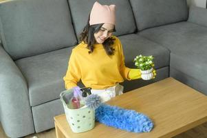 jonge gelukkige vrouw die gele handschoenen draagt en de tafel in de woonkamer afstoffen. foto