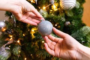 vrouw handen kerstboom versieren. kerstboom met witte en zilveren versieringen, ornamenten speelgoed en bal. moderne klassieke stijl interieur. kerstavond thuis, tijd voor feest. foto