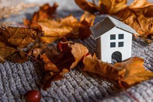 herfst achtergrond. speelgoedhuis en gedroogde oranje herfst esdoorn bladeren op grijze gebreide trui. Thanksgiving banner kopie ruimte. hygge mood koud weer concept. hallo herfst met familie foto