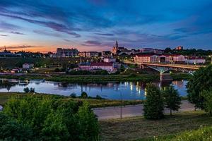 panoramisch uitzicht op de avond in de oude stad aan de oever van de brede rivier met 's avonds pluizige krullende rollende cirrostratuswolken en blauwe violetrode zonsonderganghemel als achtergrond foto