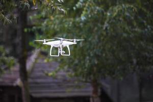 witte vliegende quadrocopter met camera op groene bosachtergrond foto