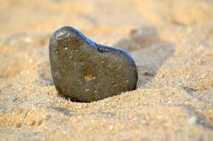 hartvorm steen tegen de achtergrond van het strand. zomer zonnige dag. liefde, huwelijk en valentijnsdag concept. mooie en interessante stenen vinden. strandvakantie foto