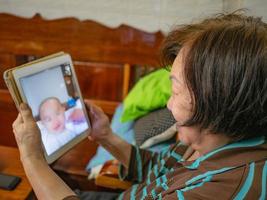 grootmoeder gebruikt haar tablet-videoconferentie om met haar kleinkind te praten foto