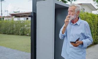 een oude oudere man die buiten een sigaret rookt, rookverslaving, slechte gewoonte. foto