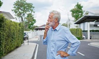 een oude oudere man die buiten een sigaret rookt, rookverslaving, slechte gewoonte. foto