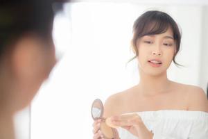 portret mooie jonge aziatische vrouw die poederdons toepast op Wang make-up van cosmetische spiegel, schoonheid van meisje met huid gezicht glimlach in de slaapkamer, gezondheid en wellness concept. foto