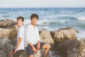 homoseksueel portret jong aziatisch paar knuffelen samen op rots of steen op het strand in de zomer, azië gay gaan toerisme voor vrije tijd en ontspannen met gelukkig in vakantie op zee, lgbt juridisch concept. foto