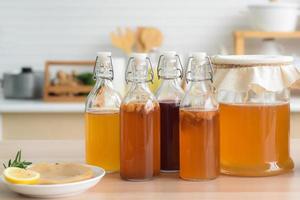 zelfgemaakte gefermenteerde rauwe kombucha thee, verschillende smaken in flessen en glazen potten mix met een vruchtensap en scoby op houten tafel in de keuken. gezonde natuurlijke probiotische drank. foto