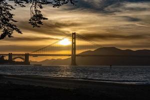 Golden Gate Bridge-zonsondergang en goudgele wolken op de achtergrond en de baai van San Francisco op de voorgrond foto