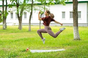 jong meisje met online training buitenshuis met behulp van laptop. pilates of yoga video les op internet. gelukkig lachend meisje dat pilatesles online oefent in de tuin buiten tijdens quarantaine. foto