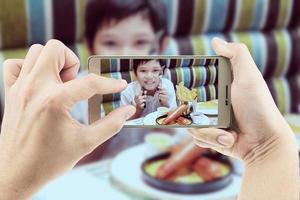 vader neemt mobiele foto van Aziatische jongen die vrolijk frietjes eet - kind met ongezond junkfoodconcept