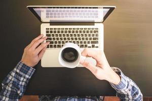mannelijke handen die op laptop werken en een kopje koffie op het bureau houden. foto