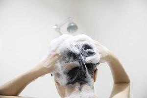 dame die shampoo gebruikt in een badkamer met spatdouche sproeiwater foto