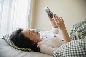 vrouw die mobiele telefoon gebruikt terwijl ze 's ochtends op bed ligt - technologie in het dagelijkse leven concept foto