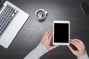 bovenaanzicht van mannelijke handen met behulp van tablet met laptop, smartphone en koffiekopje op zwarte houten tafel achtergrond. foto