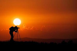 het silhouet van een professionele fotograaf is gericht op het fotograferen in een prachtige weide. foto