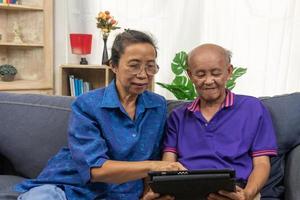 Aziatische senior met behulp van tablet online internetcommunicatietechnologie op de bank thuis. foto