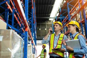 groep magazijnmedewerkers met veiligheidshelmen en reflecterende jassen met behulp van tablet, walkie talkie-radio en karton terwijl ze de voorraad en inventaris controleren in de logistiek van de detailhandel, het distributiecentrum foto