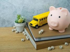 het speelgoed van de schoolbus en het spaarvarken op houten tafel voor terug naar school of onderwijsconcept foto