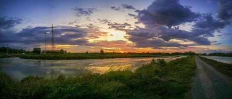 panorama de vijver reflecteert het licht van de oranje zon. de rand van het zwembad is groen en geel gras. de avondlucht voor de zonsondergang is kleurrijk. foto