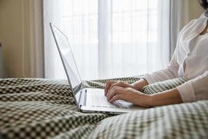 vrouw die computerlaptop gebruikt terwijl ze 's ochtends op bed wakker wordt - technologie in het dagelijkse levenconcept foto