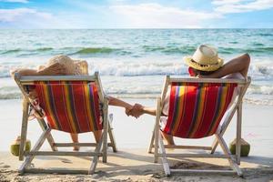 ontspannen paar gaan liggen op strand stoel met zee golf achtergrond - man en vrouw hebben vakantie op zee natuur concept foto