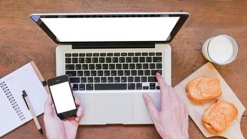 labtop, notebook, mobiele telefoon en ontbijt met handen op houten tafel foto