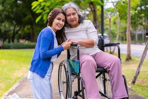Aziatische zorgvuldige verzorger of verpleegster die voor de patiënt in een rolstoel zorgt. concept van gelukkig pensioen met zorg van een verzorger en spaar- en senior ziektekostenverzekering, een gelukkig gezin foto