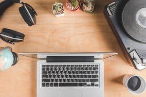 bovenaanzicht van laptop met koptelefoon, vintage draaitafel, cactus, globe en koffiekopje op houten tafel achtergrond. foto