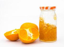 verse sinaasappel met sinaasappeljam in glazen pot op witte achtergrond. foto