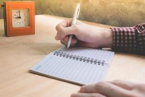 close-up van mannelijke handen schrijven wat gegevens in notitieblok op het houten bureau. foto