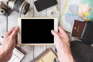 bovenaanzicht van mannelijke handen met tablet met reisuitrusting op witte houten tafel achtergrond foto