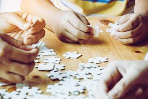 handen van een persoon klein kind en ouder spelen puzzelstukje samen op houten tafel thuis, concept voor vrije tijd met familie, spelen met de ontwikkeling van kinderen, onderwijs en plezier. foto