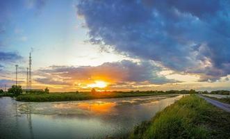 de vijver weerkaatst het licht van de oranje zon. de rand van het zwembad is groen en geel gras. de avondlucht voor de zonsondergang is kleurrijk. foto