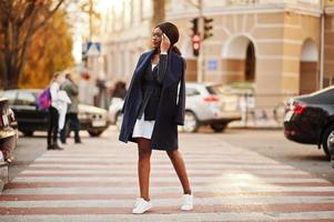 succes stijlvolle Afro-Amerikaanse vrouw in jas wandelen op zebrapad. foto