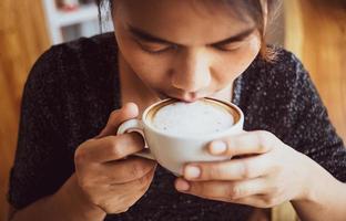 close-up van een mooi meisje dat warme koffie ruikt en drinkt met een goed gevoel in café, ze geniet van haar ochtendcappuccino met melkschuimkoffie foto