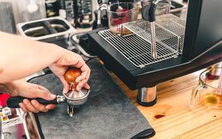 de barista perst gemalen koffie met behulp van een tamper op een houten aanrecht met een automatisch koffiezetapparaat dat in de coffeeshop is geplaatst. foto
