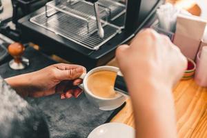 de professionele barista schenkt de melk in de roestvrijstalen mok in het warme koffiekopje om een cappuccino of latte te maken in de coffeeshop. hoe maak je cappuccino koffie? foto
