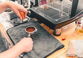 de barista perst gemalen koffie met behulp van een tamper op een houten aanrecht met een automatisch koffiezetapparaat dat in de coffeeshop is geplaatst. foto