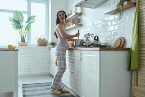 volledige lengte van gelukkige jonge vrouw in koptelefoon genietend van muziek tijdens het koken in de keuken foto