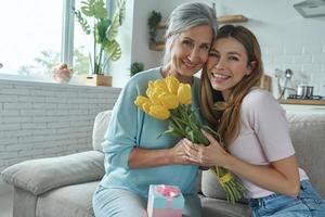 mooie senior vrouw en haar volwassen dochter zitten op de bank en houden een bos tulpen vast foto