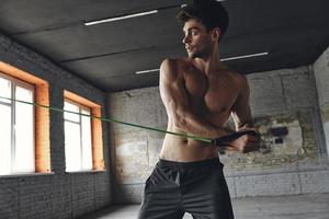 geconcentreerde jongeman die traint met elastische weerstandsband in de sportschool foto