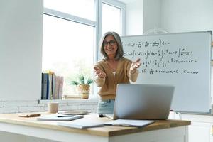 gelukkige senior vrouw gebaren terwijl ze in de buurt van het whiteboard in de klas staat foto