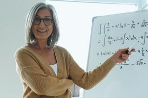 vrolijke senior vrouw die whiteboard wijst terwijl ze in de klas staat foto